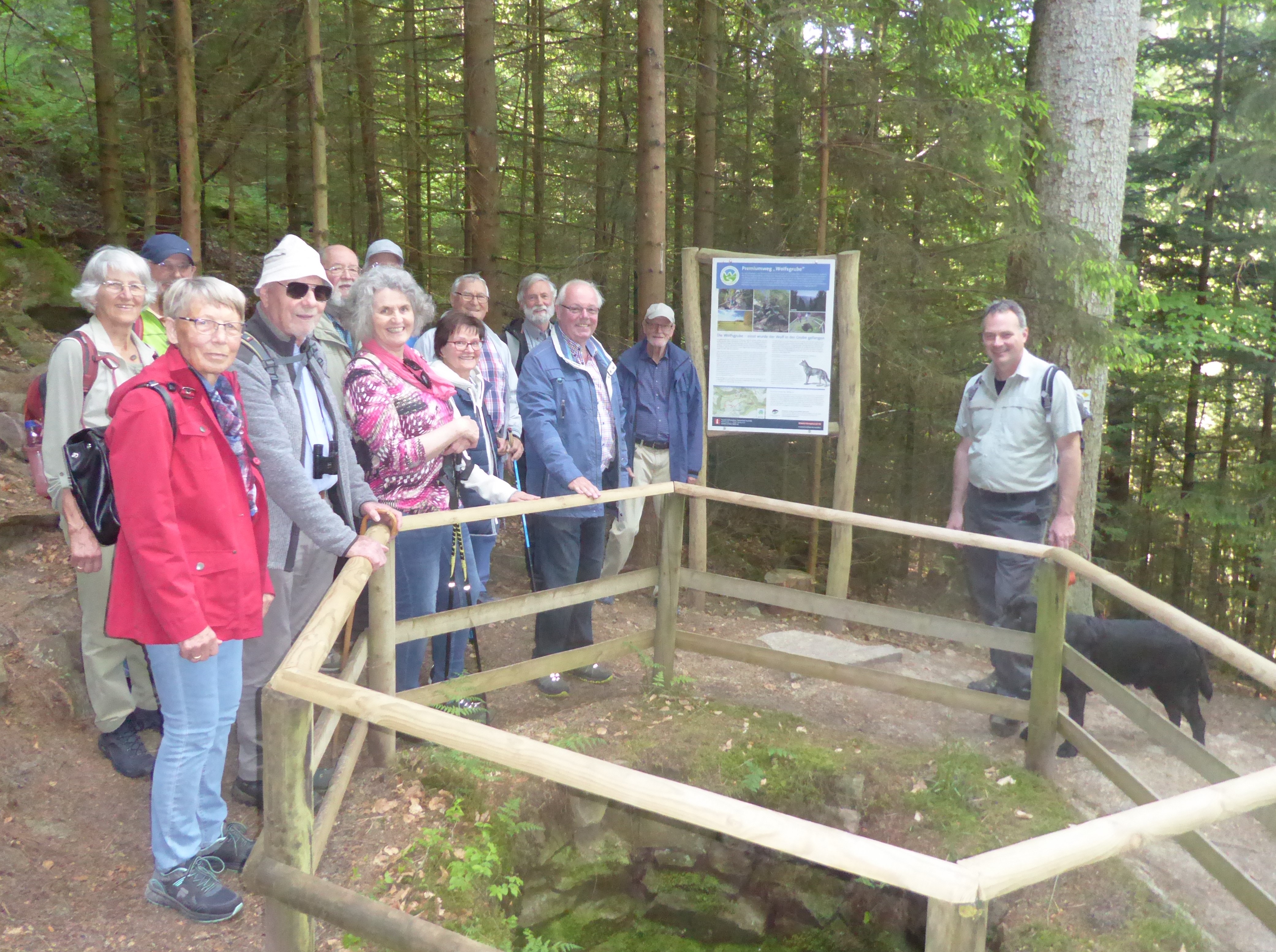 eine Gruppe Menschen steht im Wald um einen Zaun und lächelt in die Kamera
