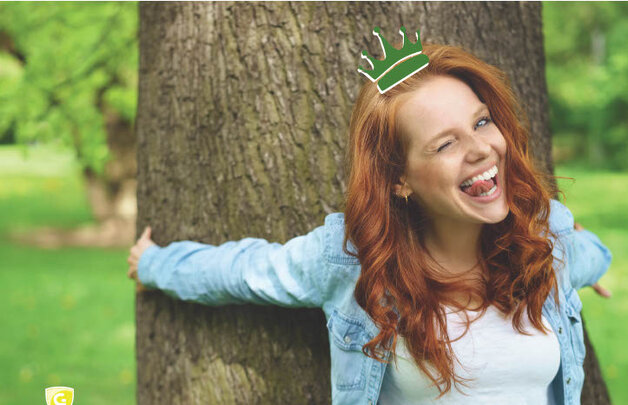 Eine junge Frau lehnt an einem Baum und lächtelt in die Kamera