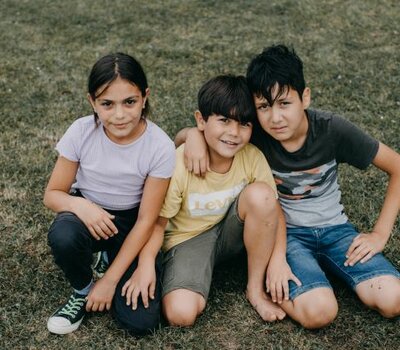 Drei Kinder sitzen zusammen auf der Wiese