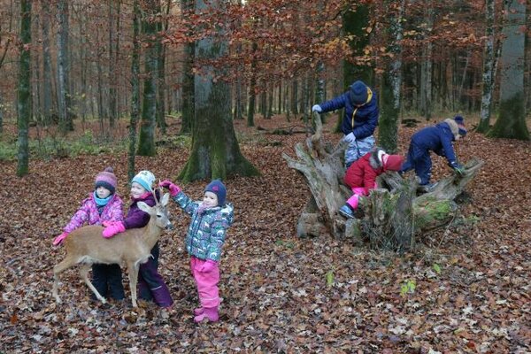 Kinder klettern auf einer Wurzel und streicheln ein Reh