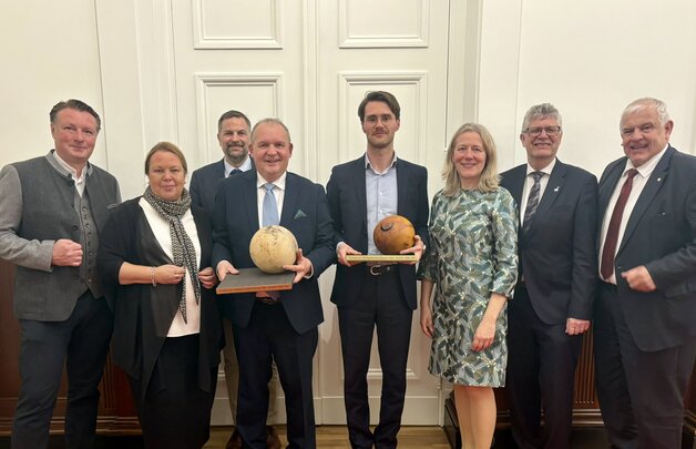 Eine Gruppe von Personen in festlicher Kleidung posiert für ein Bild. Zwei Männer in der Mitte halten jeweils eine große Holzkugel - den SDW-Ehrenpreis - in der Hand.