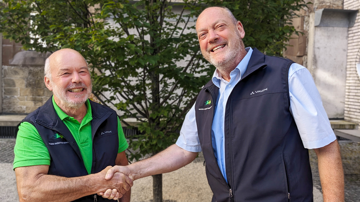 Auf dem Bild sind zwei Männer zu sehen, die sich die Hand schütteln. Der linke Mann ist Dietmar Hellmann, der das Amt des Vorstandsvorsitzenden an  Reinhold Mayer (links) übergibt.  