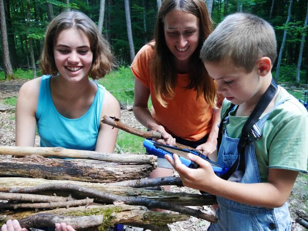 Zwei Kinder und eine Betreuerin im Wald mit Stöcken